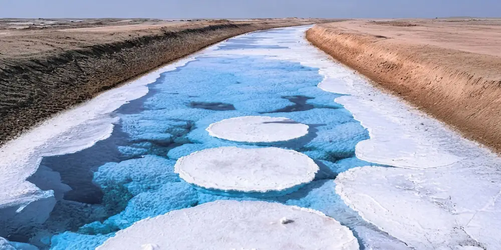 Emerald green water channel with round white crystalline salt formations cutting through the desert at Al Wathba Long Salt Lake in Abu Dhabi.