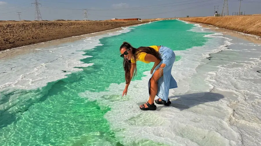 Visitor posing along the white salt crust edges of the turquoise canal at Al Wathba Long Salt Lake in Abu Dhabi.
