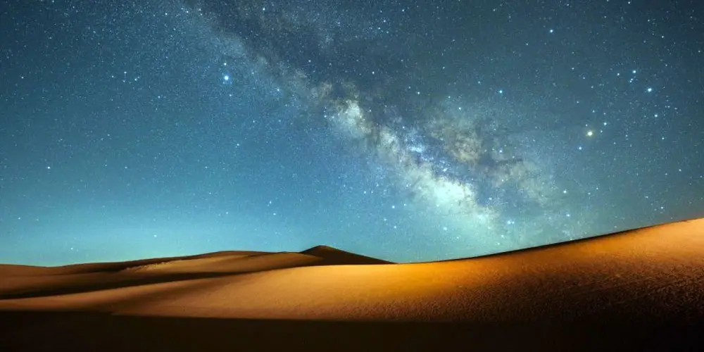 Bright core of the Milky Way stretching across a starry night sky over desert sand dunes in Abu Dhabi.