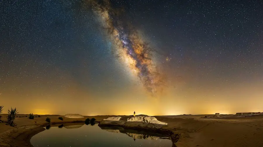 Person standing near a desert lake reflecting the brilliant Milky Way galaxy under dark skies in Abu Dhabi.