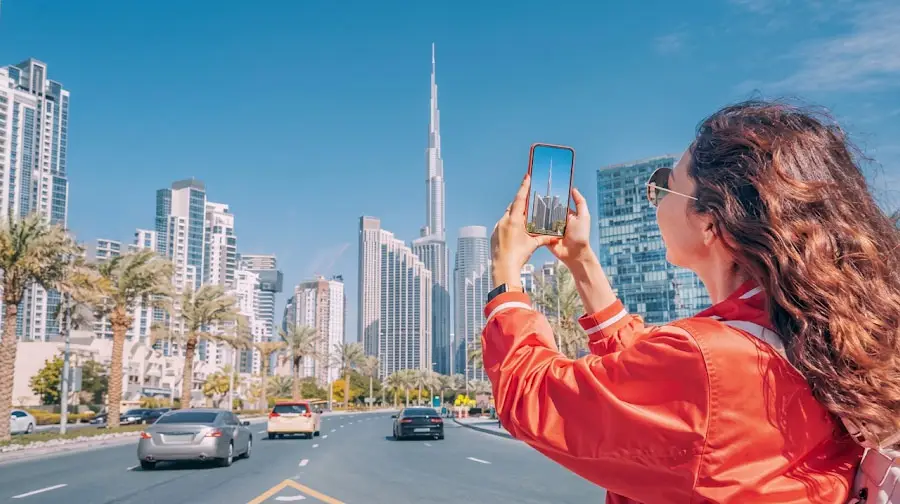 Female tourist holding up her smartphone to take a photo of the towering Burj Khalifa along a city street in Dubai.