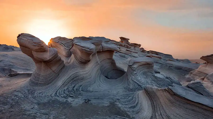 Sun flare illuminating the unique layered fossil dune formations at Al Wathba Fossil Dunes Reserve in Abu Dhabi during sunset.