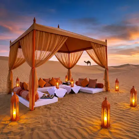 An elegant open-air gazebo with orange curtains and plush floor seating overlooks the dunes with a camel visible in the distance at sunset.