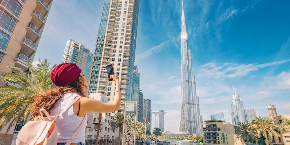 Female tourist taking a photo on her smartphone with the iconic Burj Khalifa skyscraper looming in Downtown Dubai.