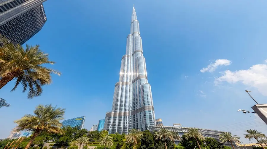 Low-angle view looking up at the towering Burj Khalifa set against a clear blue sky and palm trees in Dubai.