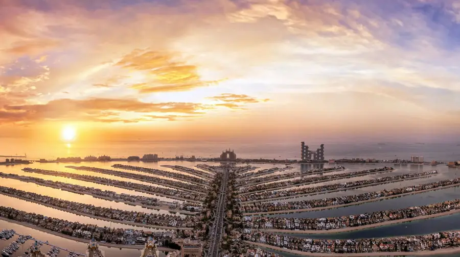 Panoramic aerial view of Palm Jumeirah luxury island fronds extending toward Atlantis The Palm during a golden sunset in Dubai.