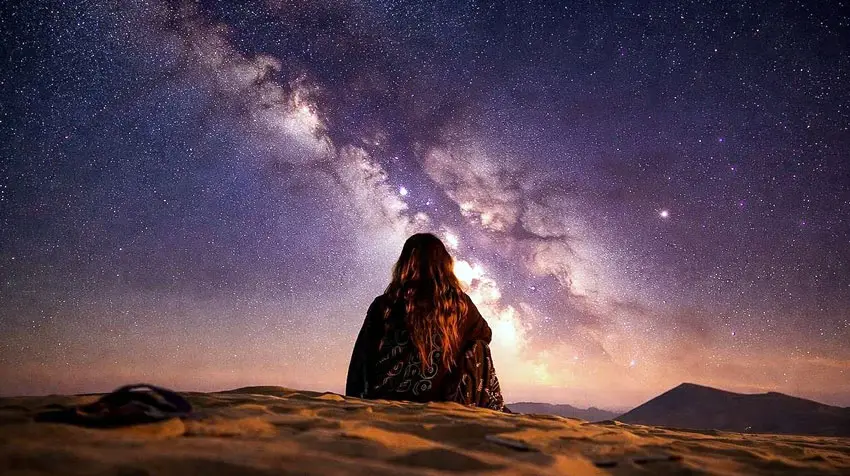 Rear view of a woman with long hair sitting on sand dunes admiring the Milky Way in Al Quaa Desert, Abu Dhabi.