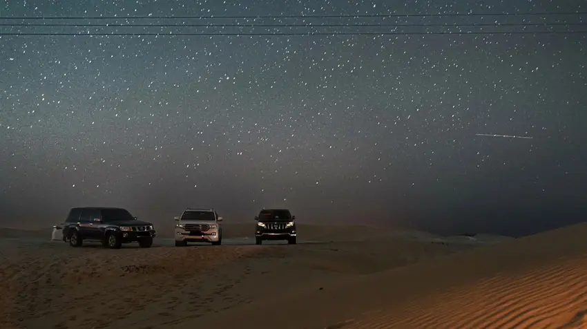 Off-road 4x4 vehicles parked on sand dunes beneath a starlit sky during a night stargazing tour in Al Quaa Desert, Abu Dhabi.