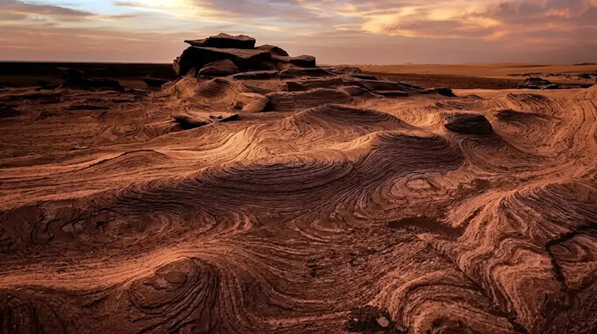 Dramatic sunset illuminating layered ancient rock formations at Al Wathba Fossil Dunes Reserve in Abu Dhabi.