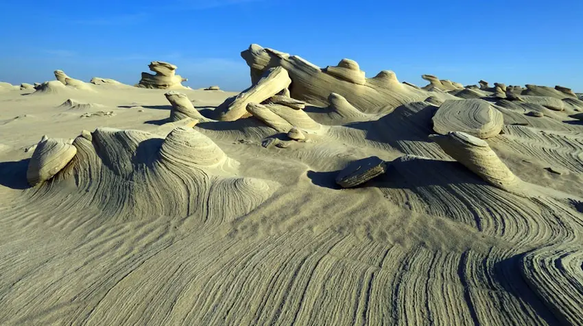 Intricate wind-carved fossilized sand dunes stretching under a clear blue sky in Al Wathba, Abu Dhabi.