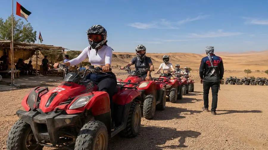 Group of riders on red quad bikes lined up at the start of a desert safari tour in Abu Dhabi, with an instructor in a Quad Bike Tours jacket standing nearby and the UAE flag visible in the background.