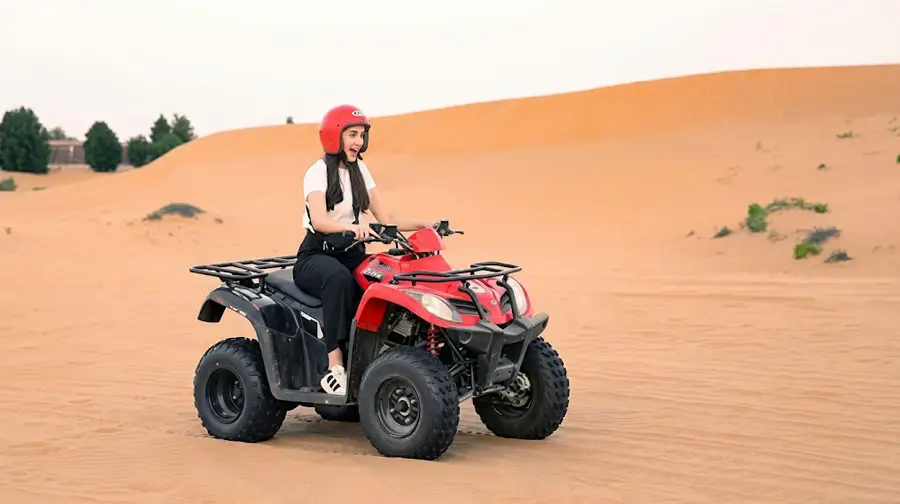 Smiling woman wearing a red helmet riding a red quad bike through the vast orange sand dunes of the Abu Dhabi Desert during a guided tour.