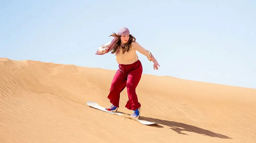 Woman sandboarding down a large sand dune in the Abu Dhabi Desert on sunrise.