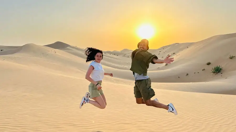 Happy couple jumping joyfully in the air on the sand dunes of Abu Dhabi Desert during a beautiful sunset.